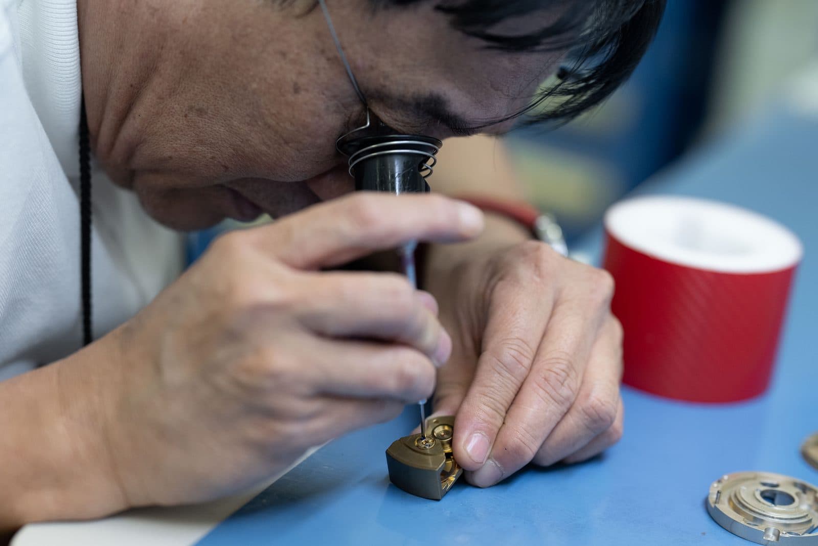 SATHOM technician working on a precision instrument with an eyeglass loupe